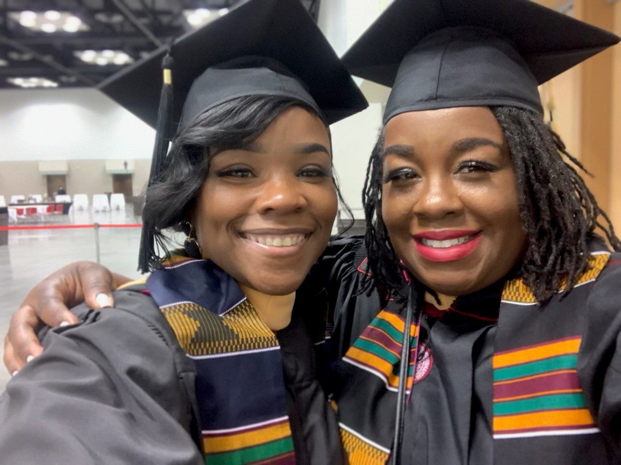 Two women wearing graduation caps and scarves.