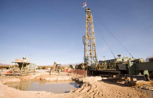 Mining site with drilling equipment, machinery, and a water pit in a desert landscape under a clear blue sky